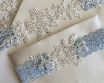Pode incluir: Dois envelopes de cetim branco com uma delicada borda de renda branca e uma borda de renda azul. Os envelopes estão sobrepostos.