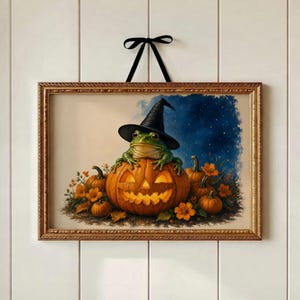 May include: A rectangular framed wall art piece featuring a green frog wearing a black witch hat, perched atop a glowing jack-o'-lantern. The scene includes several smaller pumpkins and orange flowers against a dark blue starry night sky background.