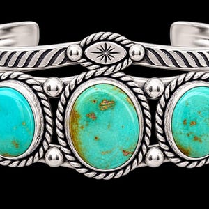 May include: A silver cuff bracelet featuring three oval turquoise stones with brown matrix patterns. The silver band is decorated with twisted rope detailing, smooth metal spheres, and a central oval element with a starburst engraving.