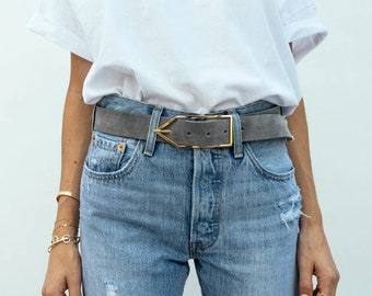 May include: A gray suede belt with a gold metal buckle. The buckle is shaped like a triangle with a point at the top.