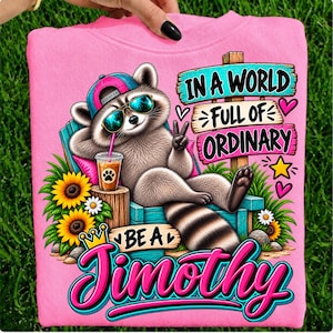 May include: A bright pink sweatshirt featuring a graphic of a raccoon wearing a pink and blue baseball cap and sunglasses, lounging in a chair with a drink. The text reads, In a world full of ordinary be a Timothy, surrounded by sunflowers.
