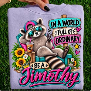 May include: A light purple sweatshirt featuring a graphic of a raccoon wearing a pink baseball cap and blue sunglasses, lounging in a chair with a drink. The text reads, In a world full of ordinary be a Timothy, surrounded by sunflowers.