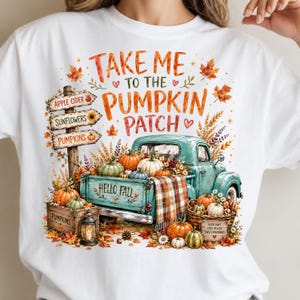 May include: A white t-shirt featuring a graphic of a teal vintage truck filled with pumpkins and a plaid blanket. The text reads "TAKE ME TO THE PUMPKIN PATCH", "HELLO FALL", and "GOOD DAYS COZY PLACES SWEET MEMORIES". A wooden sign points to apple cider, sunflowers, and pumpkins.