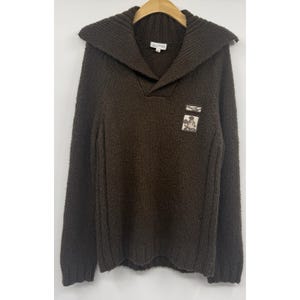 Peut inclure: Un pull en tricot à manches longues marron foncé avec un large col côtelé et une encolure en V. Le vêtement présente deux petits écussons rectangulaires sur la poitrine gauche, dont l'un affiche un motif du personnage Mickey Mouse.