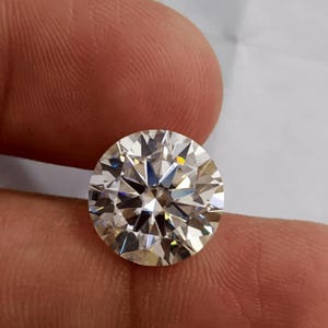 Könnte beinhalten: Ein runder Edelstein im Brillantschliff mit klarem, farblosem Aussehen und zahlreichen Facetten, die das Licht reflektieren und ein funkelndes, geometrisches Muster auf der Oberfläche erzeugen, was hohe Reinheit und präzise Symmetrie zeigt.
