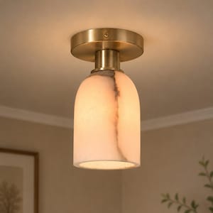 May include: A flush mount ceiling light featuring a cylindrical, translucent white stone shade with subtle grey veining. The fixture is attached to the ceiling with a circular, brushed brass metal canopy and a matching cylindrical connector.