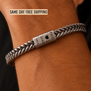 May include: A silver-toned metal wheat chain bracelet featuring three rectangular beads. The beads are engraved with the names MIA, ZOE, and PAUL, with a heart symbol between ZOE and PAUL. The bracelet has a polished finish and a secure clasp.