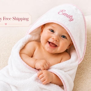 May include: A white hooded baby towel with a soft texture and pink trim. The hood features the name Emily embroidered in pink script lettering. The towel is made of absorbent fabric and is designed to wrap around a baby for drying after a bath.