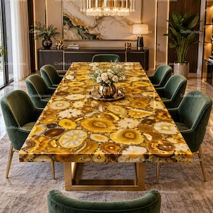 May include: A rectangular dining table featuring a polished surface made of yellow and brown agate stone slices. The table is supported by a gold-toned metal base and is surrounded by eight dark green velvet chairs with gold-toned metal legs.