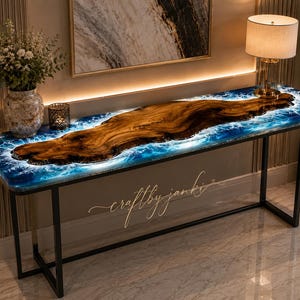 May include: A rectangular console table featuring a live edge wood slab centerpiece surrounded by blue and white ocean-inspired resin. The table has a black metal frame with four legs and includes the text craftbyjanki in cursive script.