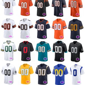 May include: A collection of twenty short-sleeved V-neck sports jerseys in various colors including white, orange, black, navy, teal, yellow, and blue. Each jersey features the number 00 or 0 on the front and is labeled with a numbered pink circle.