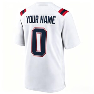 May include: A white short-sleeved sports jersey featuring the text YOUR NAME in dark blue block letters above a large dark blue number 0 with a red and white outline. The shoulders have dark blue and red stripes on a white background.