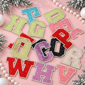 May include: A collection of varsity-style letter patches in various colors including turquoise, lime green, pink, red, black, purple, and beige. Each letter is covered in small, sparkling rhinestones and outlined with a silver beaded border.