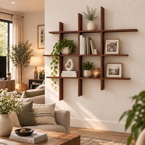 May include: A wall-mounted wooden grid shelving unit featuring multiple rectangular compartments. The shelves hold various items including potted green plants, stacked books, a white abstract sculpture, a glass candle holder, and two framed photographs.