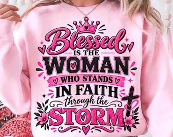 Puede incluir: Una sudadera de manga larga de color rosa claro con un estampado gráfico con el texto Blessed is the woman who stands in faith through the storm. El diseño incluye una corona rosa, letras negras, corazones rosas, flores y una cruz negra.