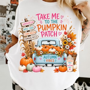 May include: A white t-shirt featuring a graphic of a light blue pickup truck filled with pumpkins and sunflowers. The text reads "TAKE ME TO THE PUMPKIN PATCH", "AUTUMN VIBES", and "PUMPKIN SPICE & EVERYTHING NICE" alongside a wooden signpost with directions.