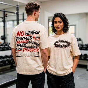 Puede incluir: Una camiseta de color crema con un gr&aacute;fico en la parte posterior con el texto 'NO WEAPON FORMED AGAINST ME SHALL PROSPER' en negro y rojo, una ilustraci&oacute;n de una corona de espinas y un gr&aacute;fico m&aacute;s peque&ntilde;o en la parte frontal.