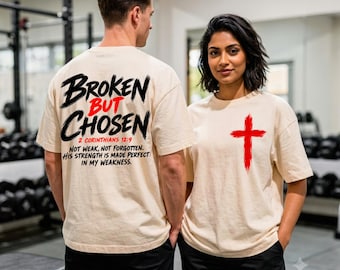 Puede incluir: Una camiseta beige con texto en negro y rojo en la parte posterior que dice Broken But Chosen 2 Corinthians 12:9 Not Weak, Not Forgotten. His Strength Is Made Perfect In My Weakness. El frente muestra un gráfico de cruz roja estilo pincelada.