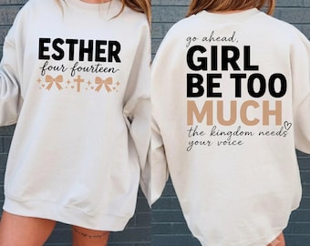 Puede incluir: Una sudadera de cuello redondo color crema con texto en negro y beige. El frente muestra ESTHER four fourteen con lazos y una cruz. La parte posterior muestra go ahead, GIRL BE TOO MUCH, y the kingdom needs your voice en negro y beige.