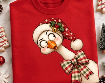 Puede incluir: Una sudadera roja de cuello redondo con el gráfico de un ganso blanco de ojos grandes y mejillas rosadas. El ganso lleva un gorro de Papá Noel rojo con estrellas blancas, un cascabel dorado y un lazo de cuadros verdes en el cuello.