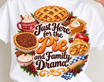 Puede incluir: Una camiseta blanca con un estampado gráfico de varias tartas, una taza de chocolate caliente, una manzana roja y un rodillo sobre un paño de cuadros azules. El texto dice "Just Here for the Pie and Family Drama", rodeado de ramas de pino.