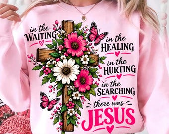 Puede incluir: Una sudadera rosa claro con un gráfico de una cruz de madera adornada con flores rosas y blancas y dos mariposas rosas. El texto dice: in the WAITING in the HEALING in the HURTING in the SEARCHING there was JESUS en color rosa.