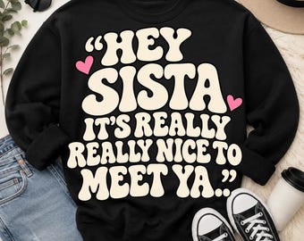 Puede incluir: Una sudadera negra de manga larga con el texto en color crema "HEY SISTA IT'S REALLY REALLY NICE TO MEET YA.." en una fuente negrita y redondeada. Dos pequeños corazones rosas están situados a la izquierda y derecha del texto.