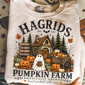 May include: A beige crewneck sweatshirt featuring a graphic print of a rustic cabin, a ghost holding a mug labeled BOO BREW, pumpkins, and a wooden wagon. The text reads HAGRIDS EST. 1981 PUMPKINS HAY RIDES HOT CIDER APPLE PICKING PUMPKIN FARM.