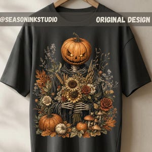 May include: A dark grey t-shirt featuring a graphic of a skeleton with a glowing jack-o'-lantern head holding a bouquet of sunflowers, roses, and wheat, surrounded by autumn leaves, mushrooms, and pumpkins. Text reads SEASONINKSTUDIO ORIGINAL DESIGN.