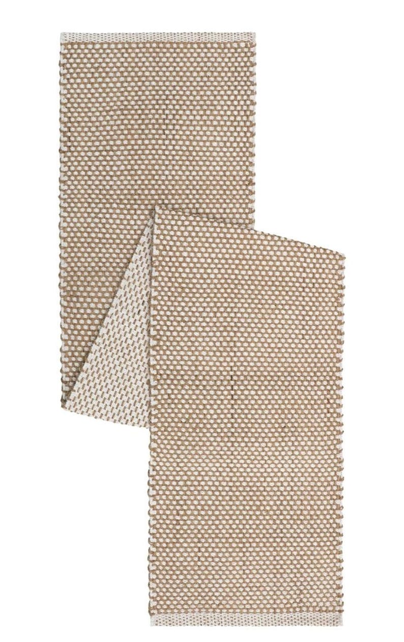 May include: A rectangular table runner featuring a woven texture with a two-tone pattern of tan and off-white threads. The fabric displays a consistent grid-like weave throughout, with finished edges and a folded section revealing the underside.