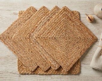 May include: A set of four square placemats crafted from natural tan braided fibers. The placemats feature a dense, woven texture with a consistent pattern throughout, arranged in a slightly overlapping stack to display the square shape and edges.
