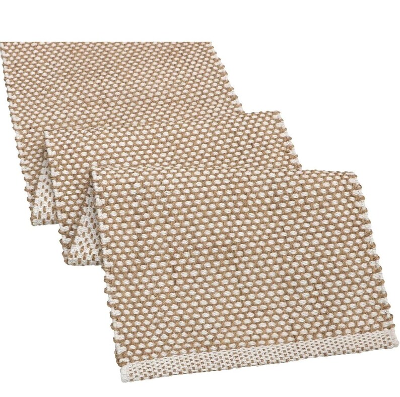 May include: A rectangular table runner featuring a woven texture with a repeating pattern of tan and off-white threads. The fabric displays a dense, grid-like weave structure with a finished edge border in a lighter off-white tone on the ends.