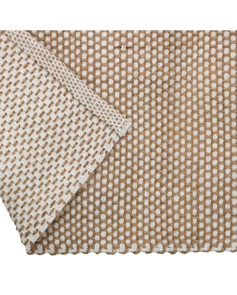 May include: A woven textile fabric featuring a grid pattern of alternating tan and white threads. The material displays a consistent, textured square weave with a folded corner edge that reveals the thickness and structure of the fabric weave.
