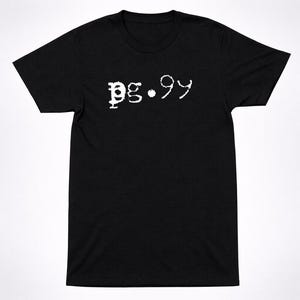 Puede incluir: Una camiseta negra de manga corta con el texto "pg.99" impreso en blanco en el pecho con una tipografía texturizada y desgastada. La prenda tiene cuello redondo y un corte estándar, con las letras blancas contrastando sobre el tejido negro.