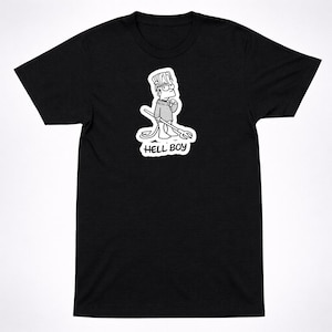 May include: A black short-sleeve t-shirt featuring a white graphic print of a cartoon character with spiky hair, wearing a sweater, holding a trident, and having a devil tail. The text HELL BOY is printed in white below the character illustration.