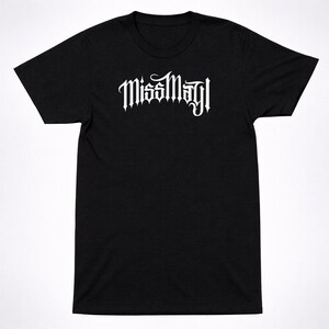 May include: A black short-sleeved t-shirt featuring the text MissMayI printed in a white, stylized, gothic-inspired font across the chest. The garment has a crew neckline and a standard fit, providing a clean look with high-contrast white lettering.