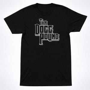 May include: A black short-sleeved t-shirt featuring the white text "THA DOGG POUND" printed in a stylized, bold, block-letter font across the center of the chest. The garment has a crew neckline and a standard fit with a plain black back.