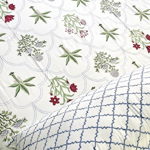 Peut inclure: Un drap de lit blanc orné d'un motif répétitif de lignes festonnées avec des fleurs dans des tons de rouge, vert et bleu. Une taie d'oreiller blanche avec un motif géométrique en treillis bleu repose sur le drap, complétant la parure.