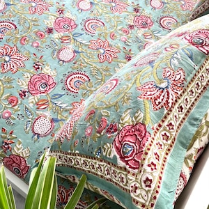 May include: A light blue bedspread and pillowcase set featuring a repeating floral pattern in shades of pink, red, and olive green. The fabric displays intricate botanical motifs with stylised flowers, leaves, and vines across the surface.