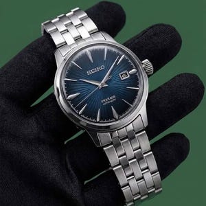 May include: A silver-tone stainless steel Seiko Presage automatic wristwatch featuring a deep blue sunray dial with silver indices, a date window at the three o'clock position, and a matching multi-link metal bracelet with a secure deployment clasp.