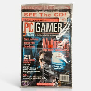 May include: A vintage PC Gamer magazine from February 1996, sealed in clear plastic. The cover features the title PC Gamer, the text Multimedia The Next Generation, and a person wearing sunglasses. It highlights 21 hard-hitting reviews including The Dig, Hexen, IndyCar Racing II, Rebel Assault II, and Beavis & Butt-Head.