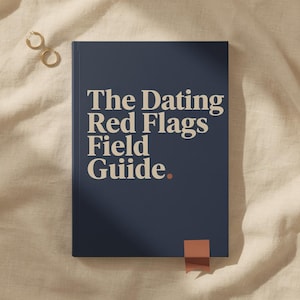 May include: A dark blue hardcover book titled The Dating Red Flags Field Guide in cream-colored serif lettering with a small terracotta dot after the word Guide. A matching terracotta bookmark ribbon extends from the bottom edge of the book.