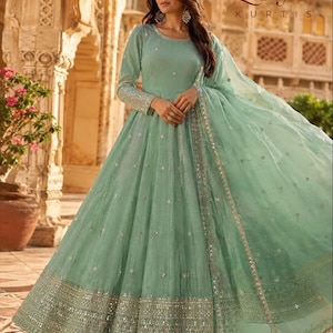 May include: A floor-length mint green Anarkali dress featuring long sleeves, a round neckline, and a flared skirt. The fabric is adorned with scattered silver embroidery and sequins, with a wide, heavily embellished silver border at the hem.