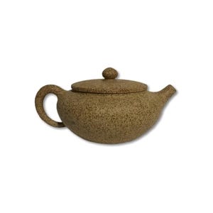 May include: A low-profile, wide-bodied teapot with a speckled, tan-coloured textured finish. The teapot features a curved handle on the left, a short spout on the right, and a circular lid with a small, rounded knob centred on the top surface.