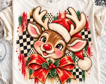 Könnte beinhalten: Ein cremefarbenes T-Shirt mit einer Grafik eines Rentiers, das eine rote Weihnachtsmannmütze trägt. Das Rentier hat eine rote Nase, rosa Wangen und eine große rote Schleife mit grünen Stechpalmenblättern. Der Hintergrund zeigt schwarz-weiße Karomuster.