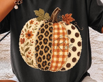 Könnte beinhalten: Ein anthrazitfarbenes T-Shirt mit einer großen Kürbisgrafik. Der Kürbis ist in vier vertikale Abschnitte unterteilt, die mit Blumen-, Leoparden-, orangefarbenen Vichy- und braunen Punktmustern versehen sind, gekrönt von grünen und braunen Blättern.