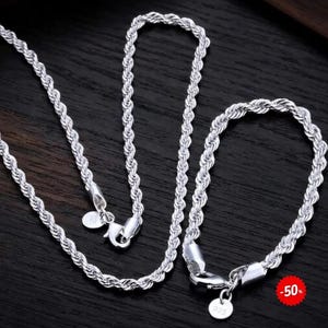 Può includere: Una collana a catena ritorta e un bracciale a catena ritorta abbinato di colore argento, entrambi dotati di chiusura a moschettone e di una piccola targhetta rotonda con impresso 925. I gioielli presentano un design intrecciato e testurizzato.