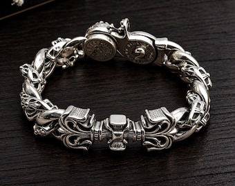 May include: A polished silver bracelet featuring intricate, ornate metalwork links and a central decorative element with symmetrical scroll patterns. The piece includes a circular clasp mechanism with engraved detailing and a sturdy, heavy-duty construction.