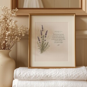 May include: A gold-framed print featuring a lavender illustration and the text 'Trust in the Lord with all your heart and lean not on your own understanding; in all your ways submit to Him, and He will make your paths straight' next to a vase.