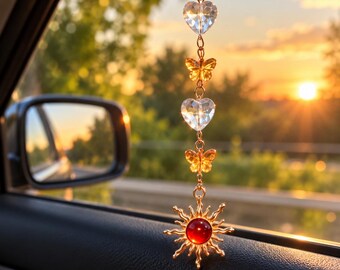 Puede incluir: Un adorno colgante para coche con una cadena dorada, dos corazones de cristal transparente, dos dijes de mariposa de color ámbar y un colgante en forma de sol con una piedra circular roja en el centro, sujeto por un mosquetón.